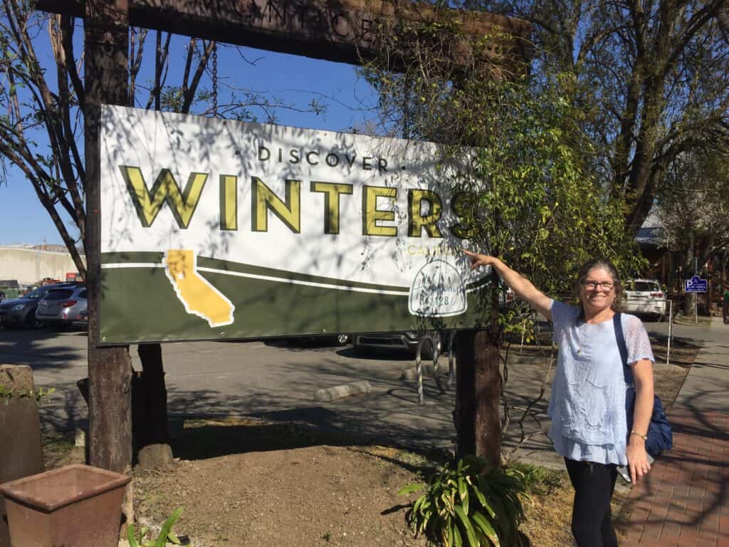 Julie from The Places Where We Go standing in front of "Welcome to Winters" sign