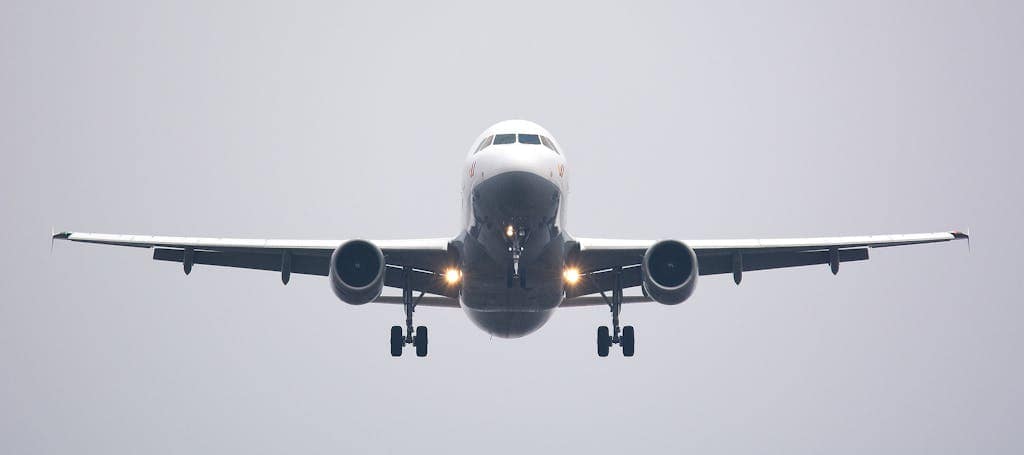 A commercial airliner captured head-on, preparing to land against a cloudy sky.