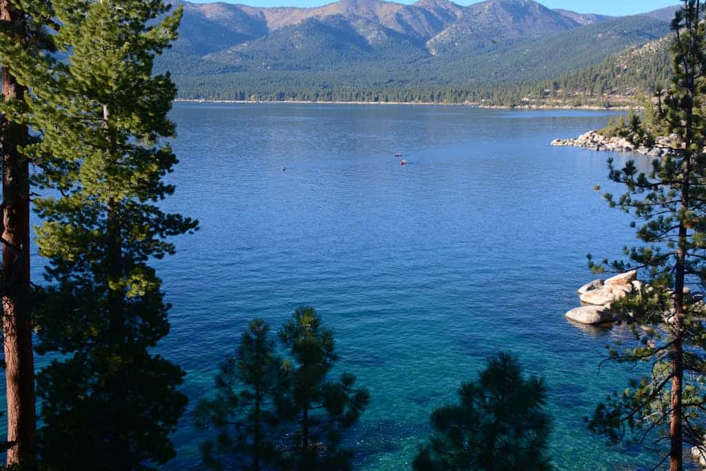 Serene view of Lake Tahoe's crystal waters, surrounded by evergreen trees and majestic mountains under a clear sky.