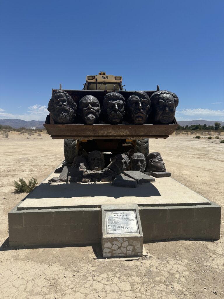 Garbage of History sculpture at Liberty Sculpture Park showing human heads underneath a tractor type of machine