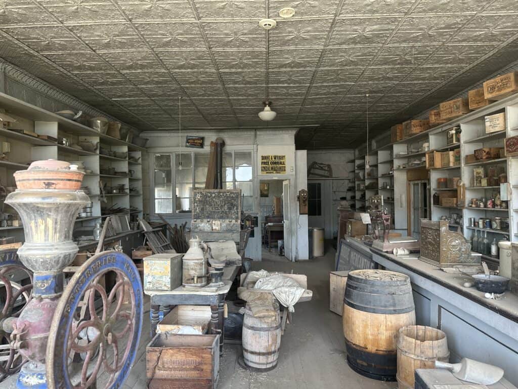 View through a store window - inside are barrels, old cash register, shelves with wooden boxes