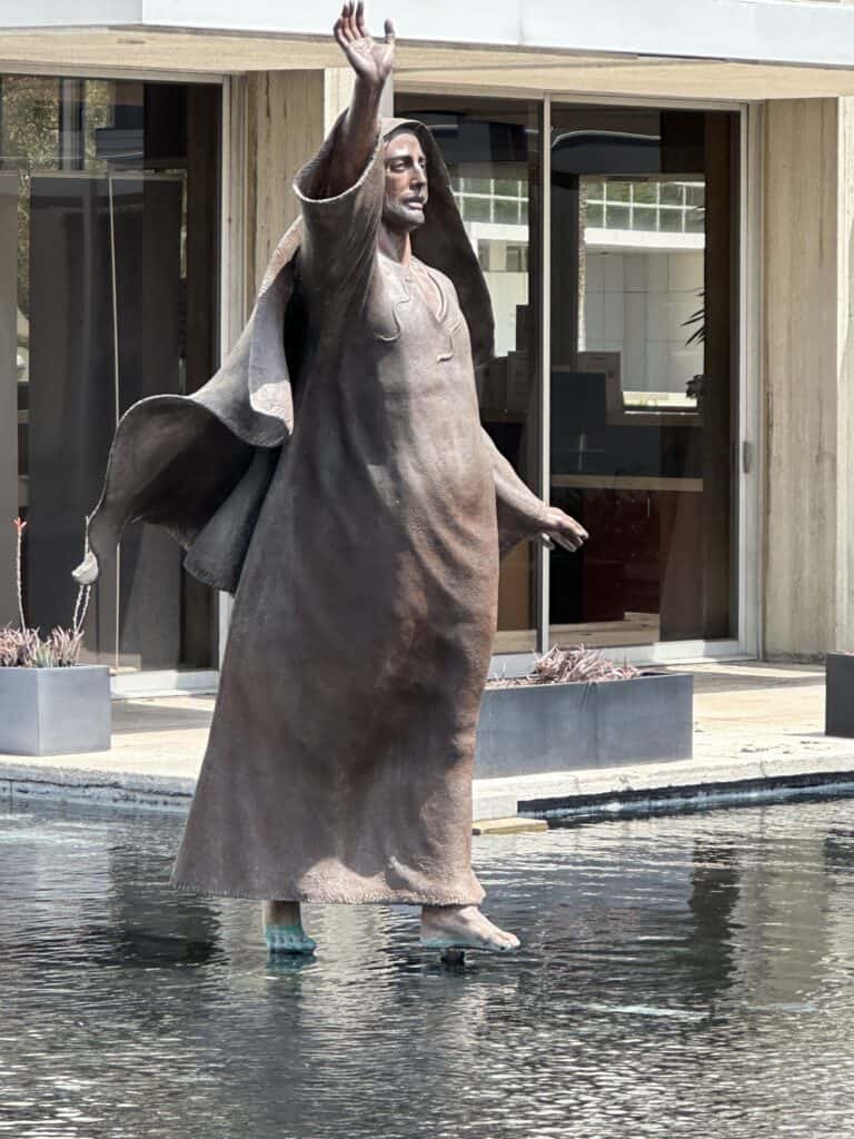 Bronze sculpture of Jesus walking on water at Christ Cathedral in Orange County, with one arm raised above a reflecting pool.